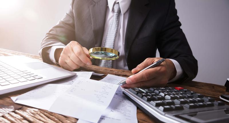 Businessperson Looking At Receipts Through Magnifying Glass