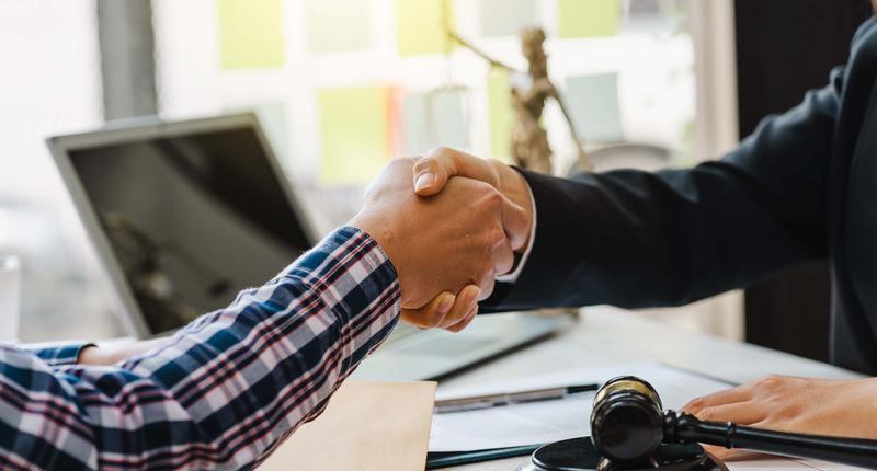 Close up of woman lawyer hand and man client shaking hand collaborate on working agreements with contract documents at the office