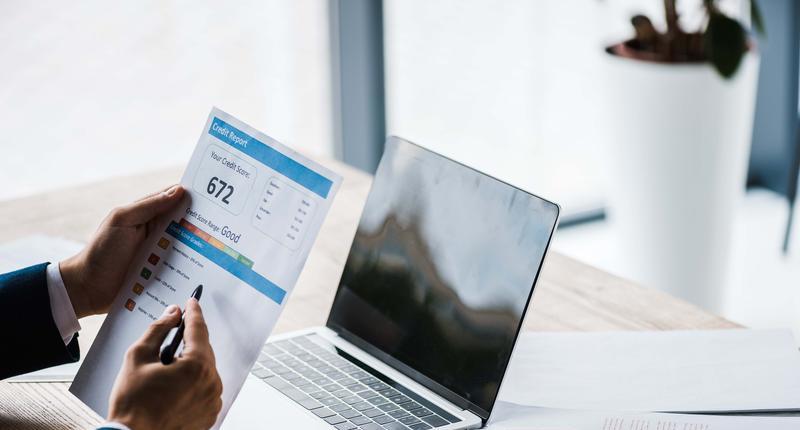 cropped view of man holding paper with credit report letters near laptop with blank screen